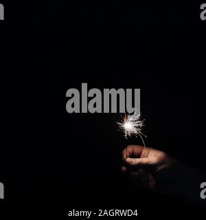 Hand with sparkler on dark background. Celebrating new year with sparkler. Hand holding sparkler on dark background. Christmas fun. New year concept Stock Photo