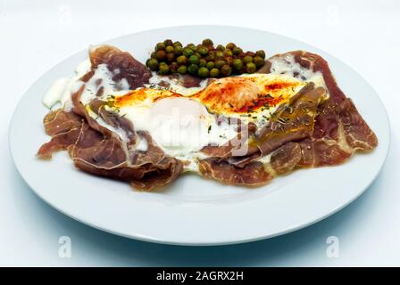 Fried eggs with ham and green peas in a white dish, isolated on white Stock Photo