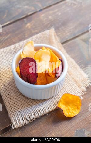 Healthy vegetable crisps made from carrots, beetroot, parsnip, sweet potato in a bowl on wooden table Stock Photo