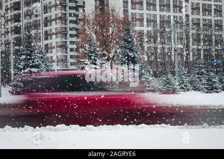 a car in motion rides along a tall building on a winter road in snow Stock Photo