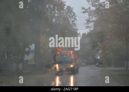 Yellow school bus with lights flashing on rainy day Stock Photo