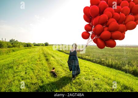 June 26, 2019 – Gainsborough, Lincolnshire, United Kingdom. An adult female stood on a grass riverbank holding a large bunch of balloons. The weather Stock Photo