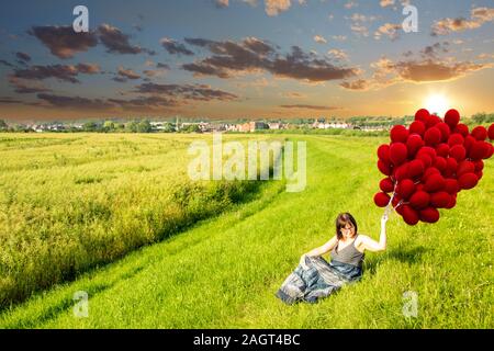 June 26, 2019 – Gainsborough, Lincolnshire, United Kingdom. An adult female stood on a grass riverbank holding a large bunch of balloons. The weather Stock Photo