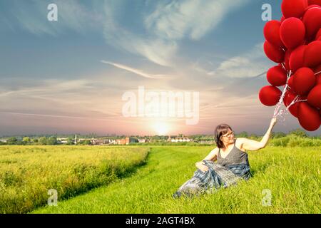 June 26, 2019 – Gainsborough, Lincolnshire, United Kingdom. An adult female stood on a grass riverbank holding a large bunch of balloons. The weather Stock Photo