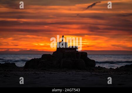 Sun setting in the ocean behind a silhouette of a sand castle at a beach in northern France Stock Photo