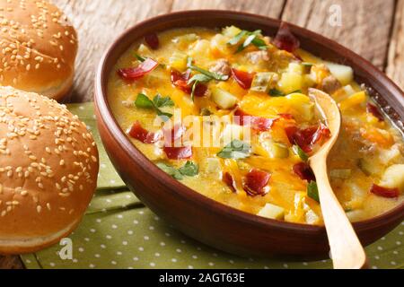 Homemade cheeseburger soup close-up in a bowl with buns on the table. horizontal Stock Photo