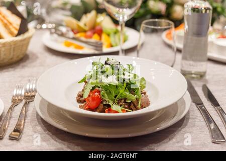 Fresh salad with tomatoes, beef, lettuce and arugula on plates in restaurant Stock Photo