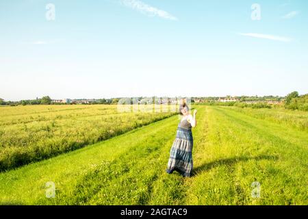 June 26, 2019 – Gainsborough, Lincolnshire, United Kingdom. An adult female stood on a grass riverbank holding her arm in the air. The weather is sunn Stock Photo