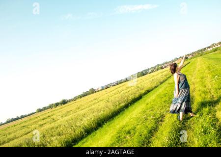 June 26, 2019 – Gainsborough, Lincolnshire, United Kingdom. An adult female stood on a grass riverbank holding her arm in the air. The weather is sunn Stock Photo