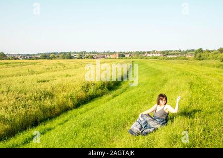 June 26, 2019 – Gainsborough, Lincolnshire, United Kingdom. An adult female stood on a grass riverbank holding her arm in the air. The weather is sunn Stock Photo