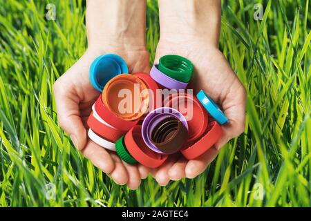 Plastic caps from different bottles in hands on a background of grass, close-up. Concept on the theme of respect for nature and environmental protecti Stock Photo