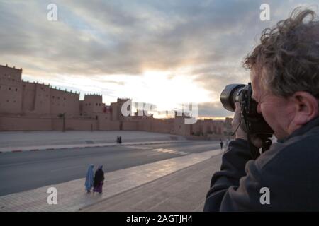 Morocco, Quarzazate, man taking photograph towards the ancient Kasbah in Quarzazate at sunset. Stock Photo