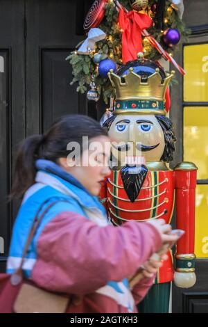 Central London, London, 21st Dec 2019. A woman walks past a large carved wooden nut-cracker in Argyll Street. Shops, hotels, restaurants and residences have all decked the halls and decorated their entrances in festive splendor around Mayfair, Oxford Street and Regent Street in London in the last few days before Christmas. Stock Photo