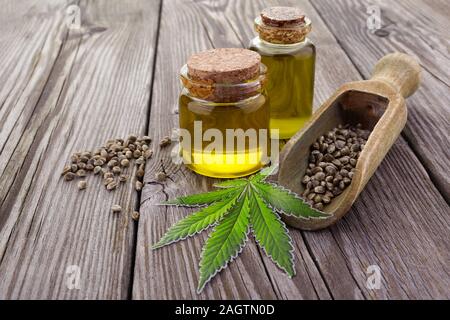 hemp seed in wooden spoon, oil in glass jar, green leaves cannabis on wooden background Stock Photo