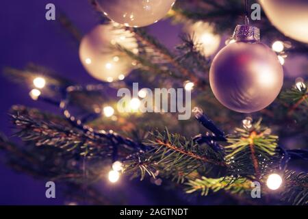 Closeup of Christmas ornaments and lights on real Christmas tree and purple background. Christmas, holidays and seasonal greetings concepts. Stock Photo