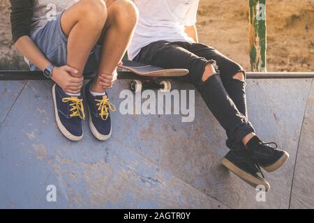 Close up of two young boys sitting on half pipe ramp, after nice tricks and jumps at the skatepark. Trendy teenagers enjoying free time at the skate p Stock Photo