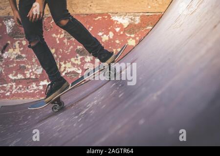 Close up view of tennager's feet riding a skateboard making tricks on half pipe. Trendy young skater enjoying outdoors at the skatepark with skate boa Stock Photo