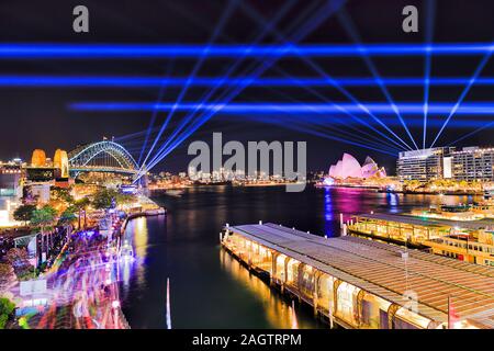 Bright blue laser beams in dark sky over Sydney city harbour waterfront around Circular quay and the Rocks during annual light show with blurred crowd Stock Photo