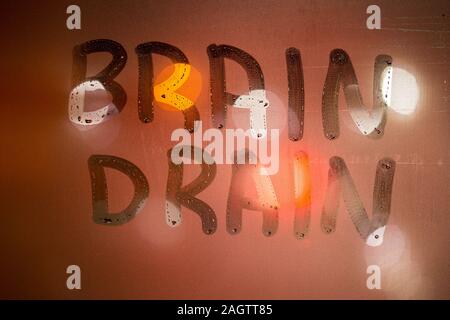 the words brain drain written on night wet window glass close-up with blurred background in orange colors Stock Photo