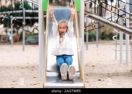 Happy little girl having fun on slide in park . Stock Photo