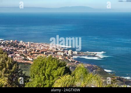 View over green treetops to  the north coast and Puerto de la Cruz on the island of Tenerife with dark blue Atlantic Ocean and a blue sky. Stock Photo