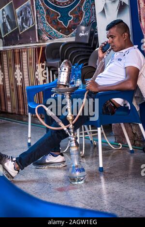 November 2019, LUXOR, EGYPT - Moslem man smokes pipe and talks on cell phone of Egypt go shopping at Luxor Souq Stock Photo