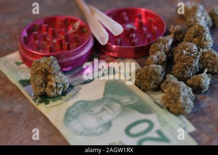 A grinder, pre rolled joints, canadian money, and weed Stock Photo