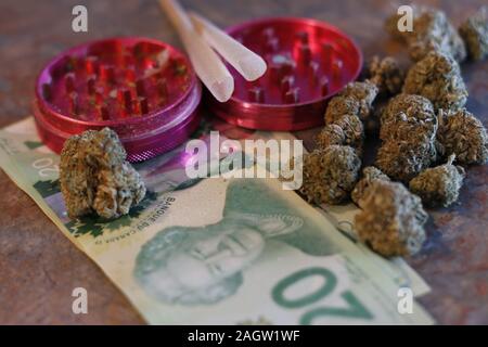 A grinder, pre rolled joints, canadian money, and weed Stock Photo