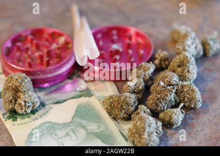 A grinder, pre rolled joints, canadian money, and weed Stock Photo