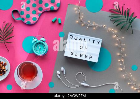 Text 'Quality of sleep', creative concept. Sleeping mask in polka dots, small alarm clock, earphones and earplugs. Pills and capsules with sleep remed Stock Photo