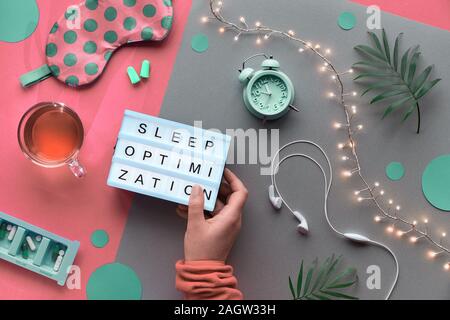 Healthy night sleep creative concept. Sleeping mask, alarm clock, earphones, earplugs, tea and pills. Split two tone pink craft paper background with Stock Photo