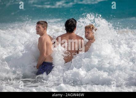 Palm Beach, Florida, USA. 21st Dec, 2019. SAM SPIEGEL, left, DEOK JUN LEE, and BAILEY SPIEGEL, right, play in the rough surf in Palm Beach, Florida. A low-pressure system is developing in the Gulf of Mexico and could cause storms -- and even tornadoes -- in southern Florida starting Saturday. The National Weather Service in Miami is predicting severe storms, heavy rain and flooding through Sunday. Credit: Greg Lovett/ZUMA Wire/Alamy Live News Stock Photo