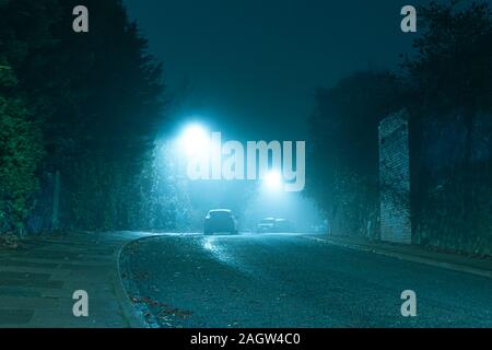 An dark mysterious eerie, English road with street lights on an atmospheric foggy winters night. UK Stock Photo