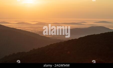 View from overlook at sunrise with fog and mountain peaks in the distance and rising sun Stock Photo