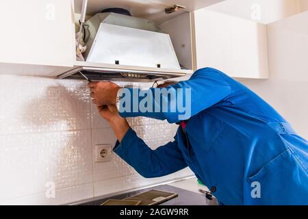 Mature repairman iin blue uniform is fixing the kitchen ventilation Stock Photo