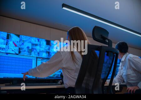 Group of Security data center operators (administrators) working in a group at a CCTV monitoring room while looking at multiple monitors ( computer sc Stock Photo