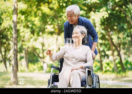 senior asian man and wheelchair bound woman relaxing outdoors in park Stock Photo