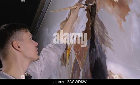 Artist designer draws an eagle on the wall. Craftsman decorator paints picture with acrylic oil color. Painter painter dressed in paint coat. Indoor. Stock Photo
