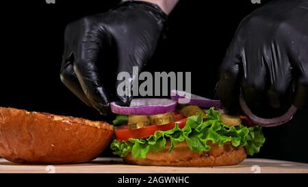 Craft burger is cooking on black background. Consist: sauce, lettuce, tomato, red onion, pickle, cheese, bacon, air bun and marbled meat beef. Stock Photo
