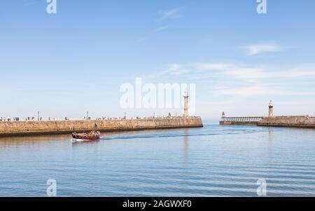 The east and west piers at the entrance to the seaside town of Whitby in Yorkshire, Northern England as a tourist boat arrives in the harbour. Stock Photo