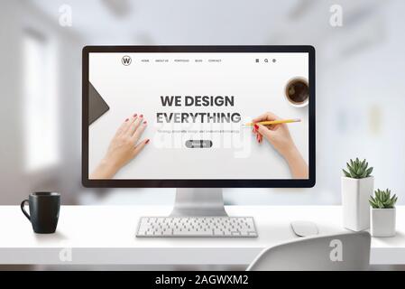 Web design studio concept with modern agency web page on computer display. Office, studio desk with cup of coffee and plants beside Stock Photo
