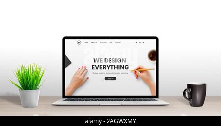 Web design studio concept. Latop with modern, flat design agency web page on desk. Plant and cup of coffee beside Stock Photo