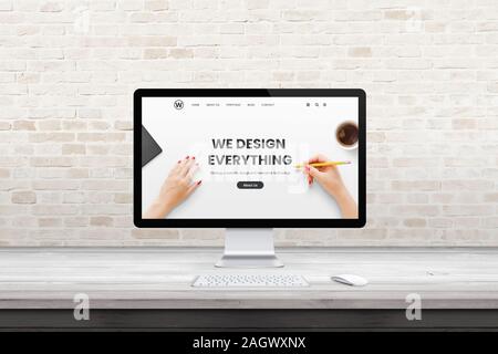 Modern computer display with web design agency page on office, studio desk. Flat design concept. Modern flat design interior with brick wall in backgr Stock Photo