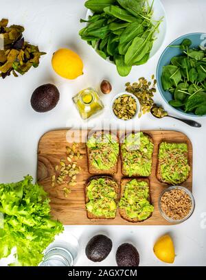 Sandwiches with avocado guacamole with pumpkin seeds and wheat seedlings on a wooden board on the table. Top view. Stock Photo