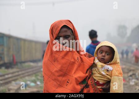 Winter cold tejgoan railway station,21dec2019 tejgoan railway stationDhaka Bangladesh.An elderly woman holds the baby in her arms and wraps the baby Stock Photo