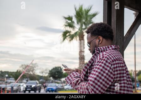 Athens, Greece - November 30 2019: Afro american man looking at the phone in summer against the palm tree with headphones Stock Photo