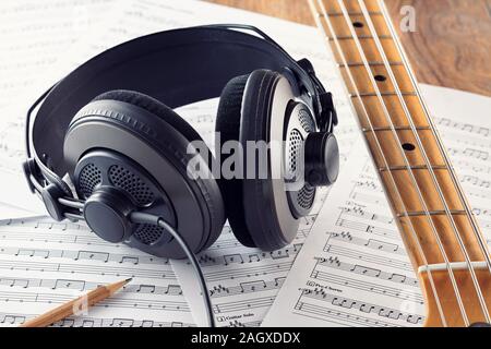 Professional studio headphones and bass guitar neck on music sheets background. Concept of music recording or composing. Close up view. Stock Photo