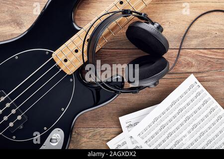 Black bass guitar with headphones and sheet music on wooden table. Practice, compose or produce music.. Stock Photo