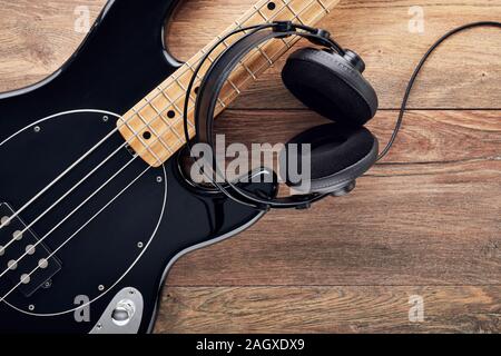 Black bass guitar with headphones on wooden table. Stock Photo