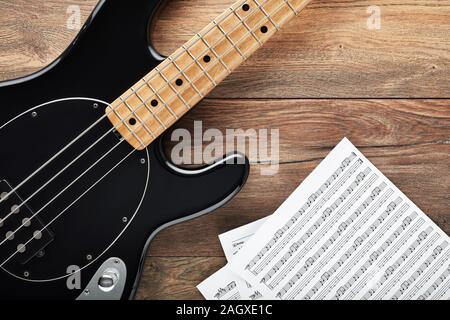 Black bass guitar with headphones and sheet music on wooden table. Music production, composing or practicing. Stock Photo